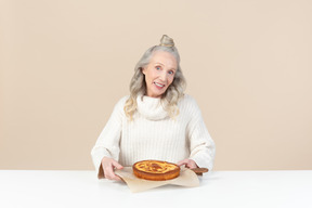 Elegante alte frau mit einem frisch gebackenen kuchen zufrieden