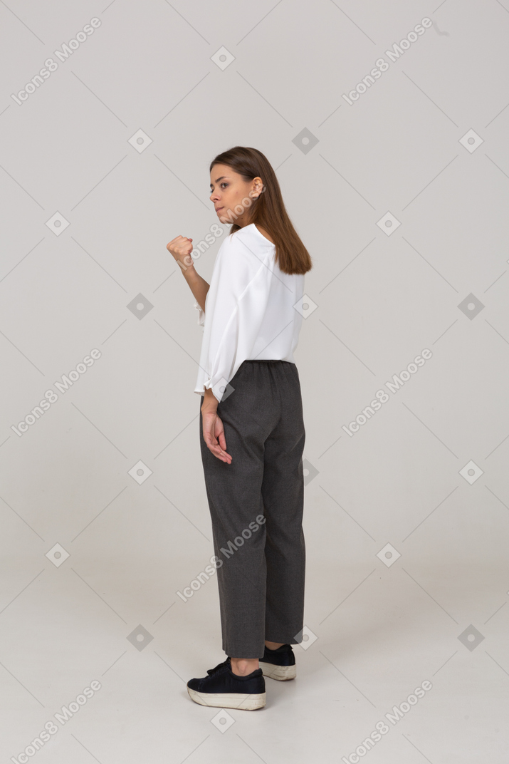 Vue de trois quarts arrière d'une jeune femme en colère en tenue de bureau serrant le poing