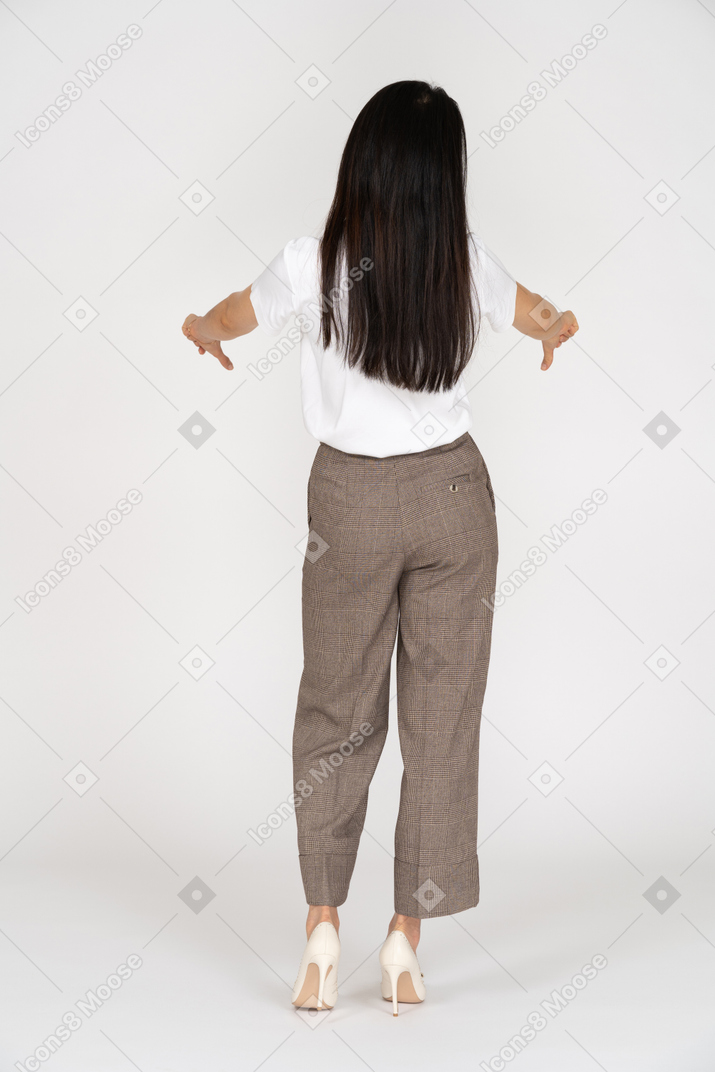 Vista posteriore di una giovane donna in calzoni e maglietta che mostra i pollici verso il basso