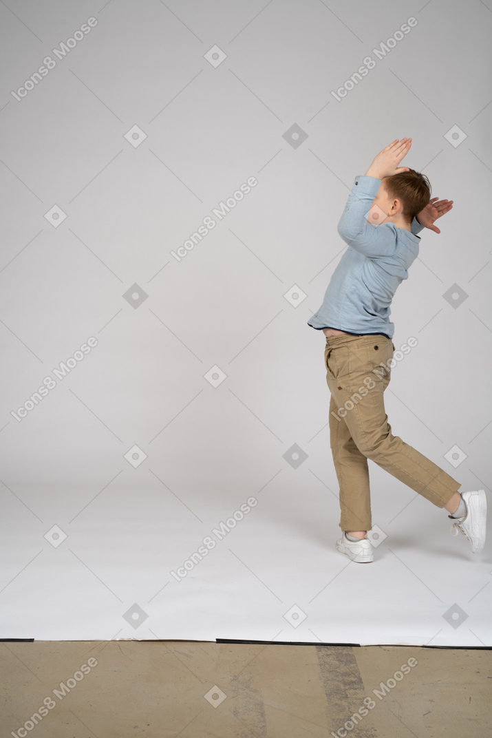 Vue latérale d'un adolescent qui court avec ses mains en l'air