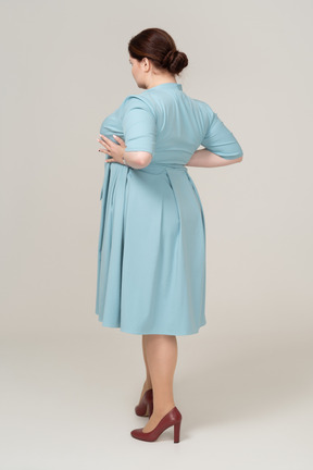 Rear view of a woman in blue dress standing with hands on hips