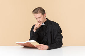 Catholic priest sitting at the table and reading a bible