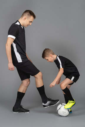 De cuerpo entero de un joven entrenando a un niño pequeño cómo jugar fooyball