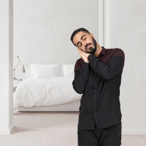 A man standing in a sleeping position in front of a white bed