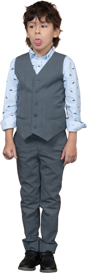 Vista frontal de un chico lindo en traje gris mostrando la lengua y mirando a un lado