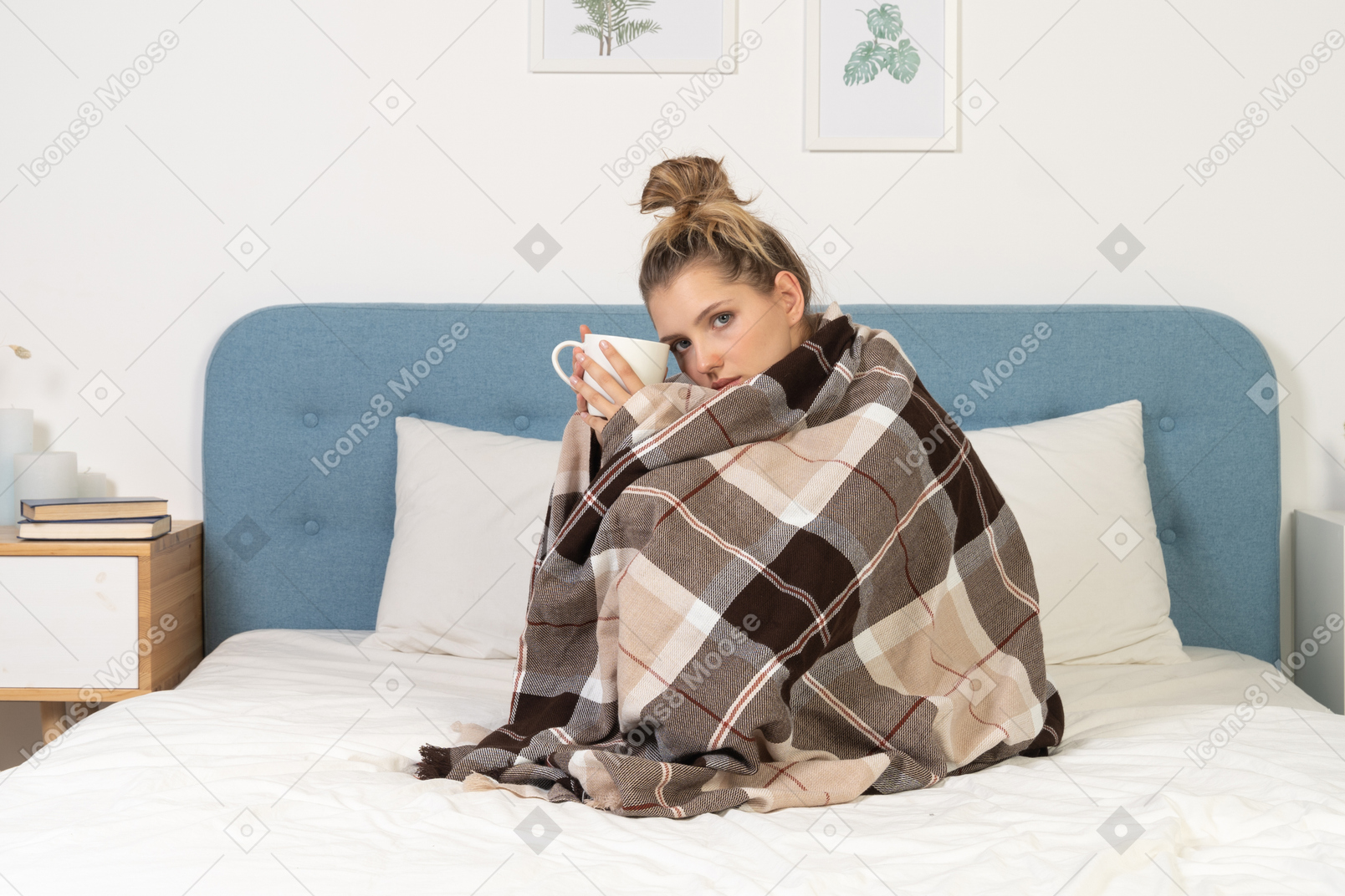 Side view of an ill young lady wrapped in checked blanket in bed holding a cup of tea