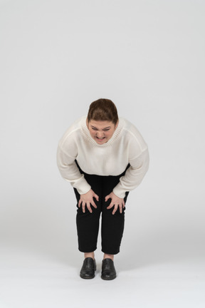 Женщина больших размеров в белом свитере трогает больные колени