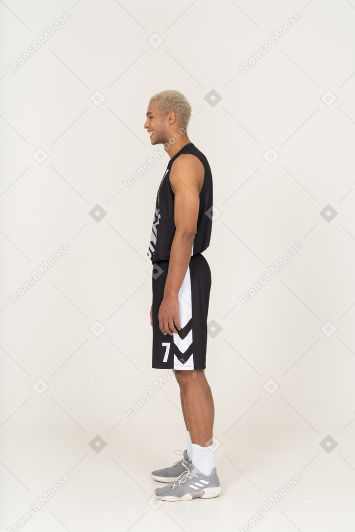 Vista laterale di un giovane giocatore di basket maschile che ride in piedi immobile