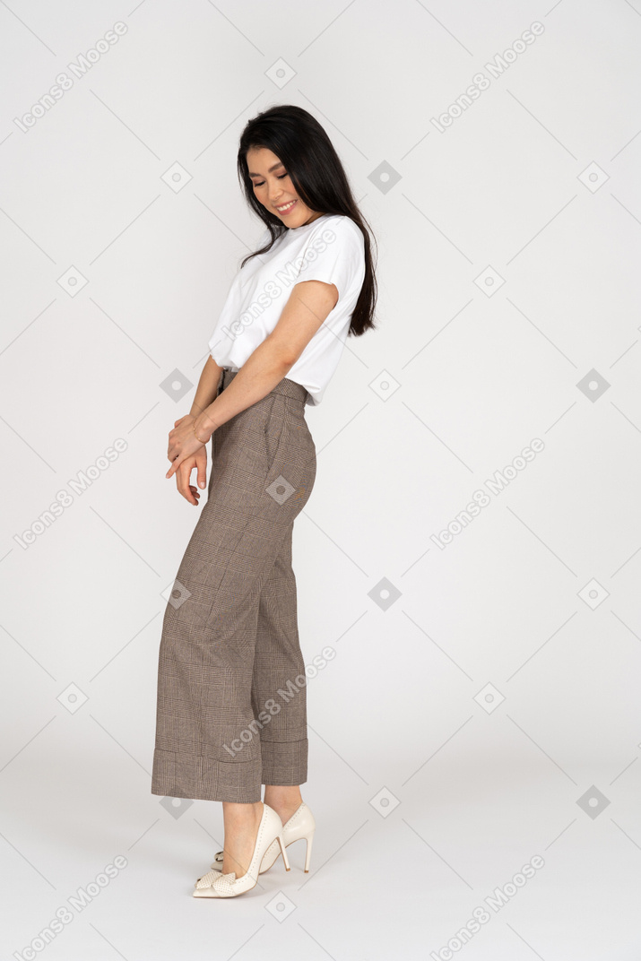 Vista lateral de uma jovem tímida e sorridente de calça e camiseta de mãos dadas