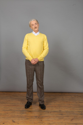 Front view of a confused old man holding hands together and wearing yellow pullover