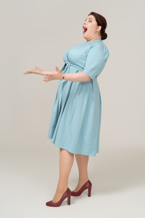 Впечатленная женщина в синем платье позирует в профиль