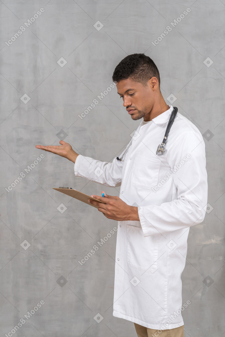 Doctor con estetoscopio mirando el portapapeles y apuntando a algo.