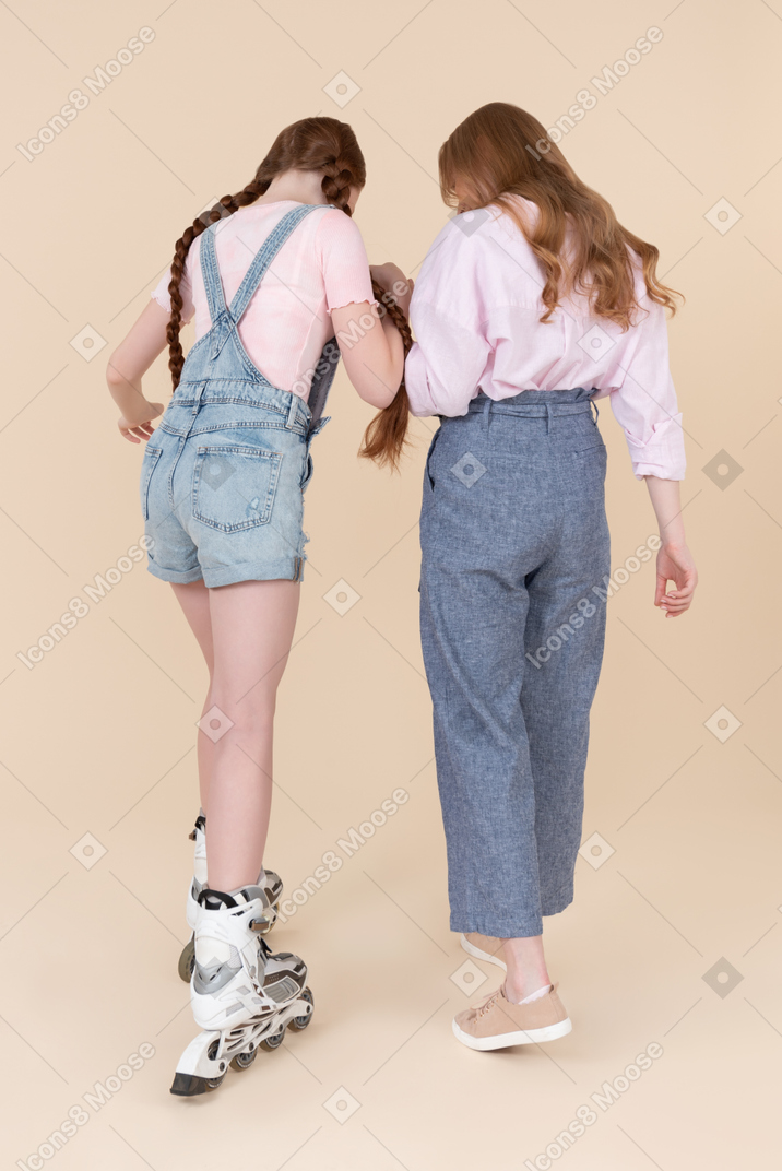 Young woman helping teen girl to ride on rollerblades