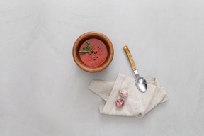 A bowl of gazpacho, some garlic and a spoon