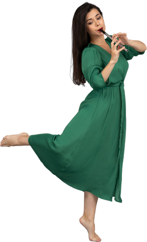 Vista laterale di una giovane donna scalza in abito verde che suona il flauto