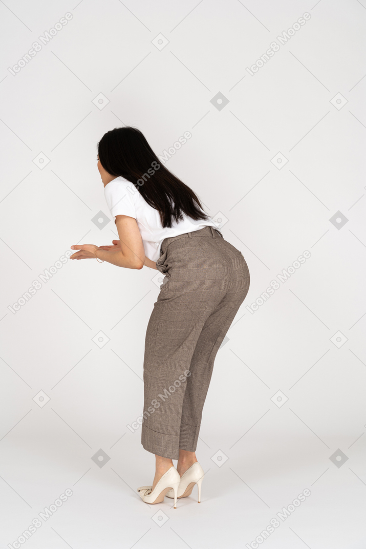 Vista posteriore di tre quarti di una giovane donna interrogativa in calzoni e maglietta che alza le mani e si china