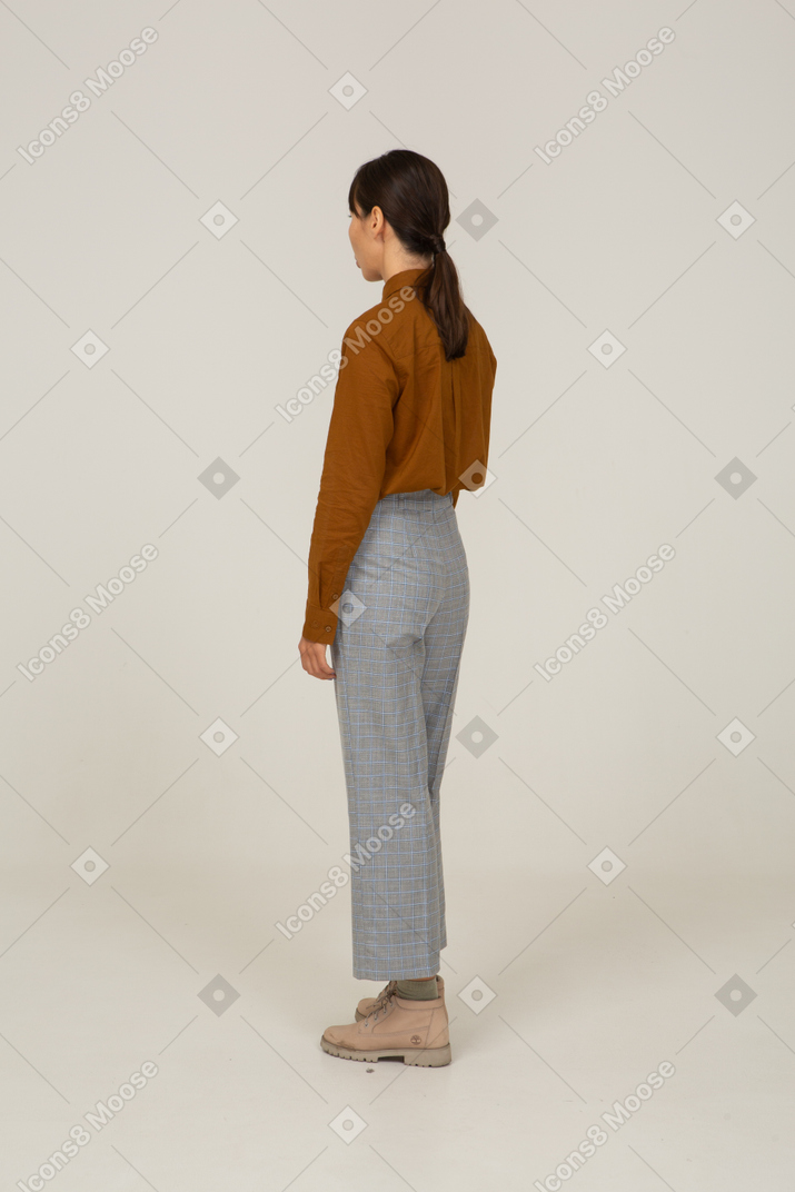 Vista traseira de três quartos de uma jovem mulher asiática fazendo beicinho travessa de calça e blusa