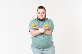 Overweight man in sportswear holding hands crossed and holding apples