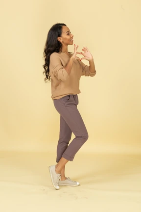 Side view of a dark-skinned young female showing heart gesture