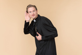 Catholic priest holding hand close to an ear and listening carefully