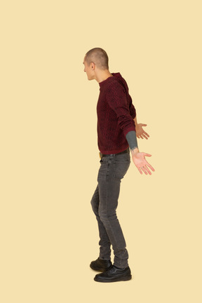 Side view of a young surprised man in red pullover outspreading his hands