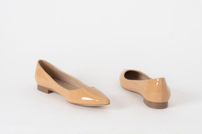 Una foto de un par de zapatos de tacón bajo de laca beige en el suelo