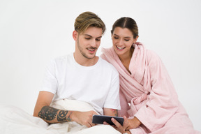 Couple sitting in bed and looking at smartphone