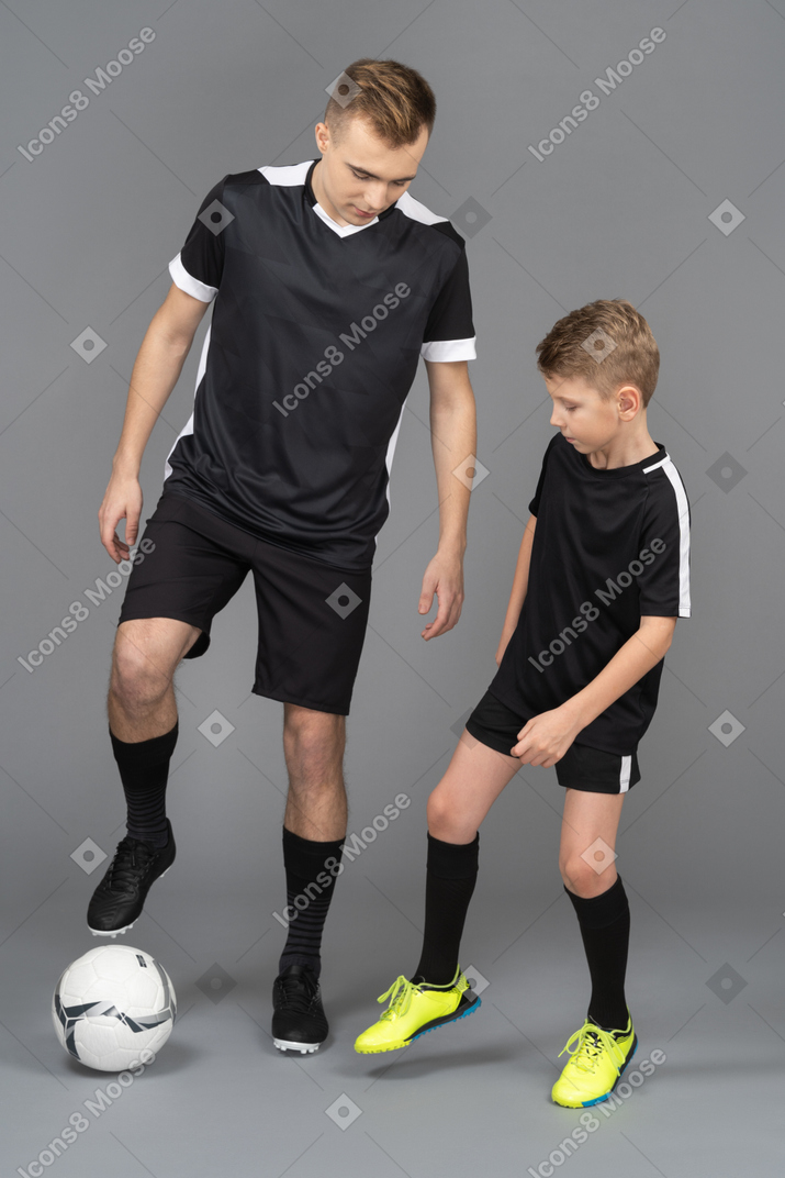 In voller länge von einem jungen mann, der einem kleinen jungen beibringt, wie man fußball spielt