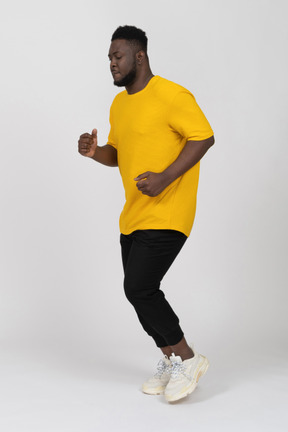 Vista di tre quarti di un giovane uomo dalla pelle scura che corre in maglietta gialla