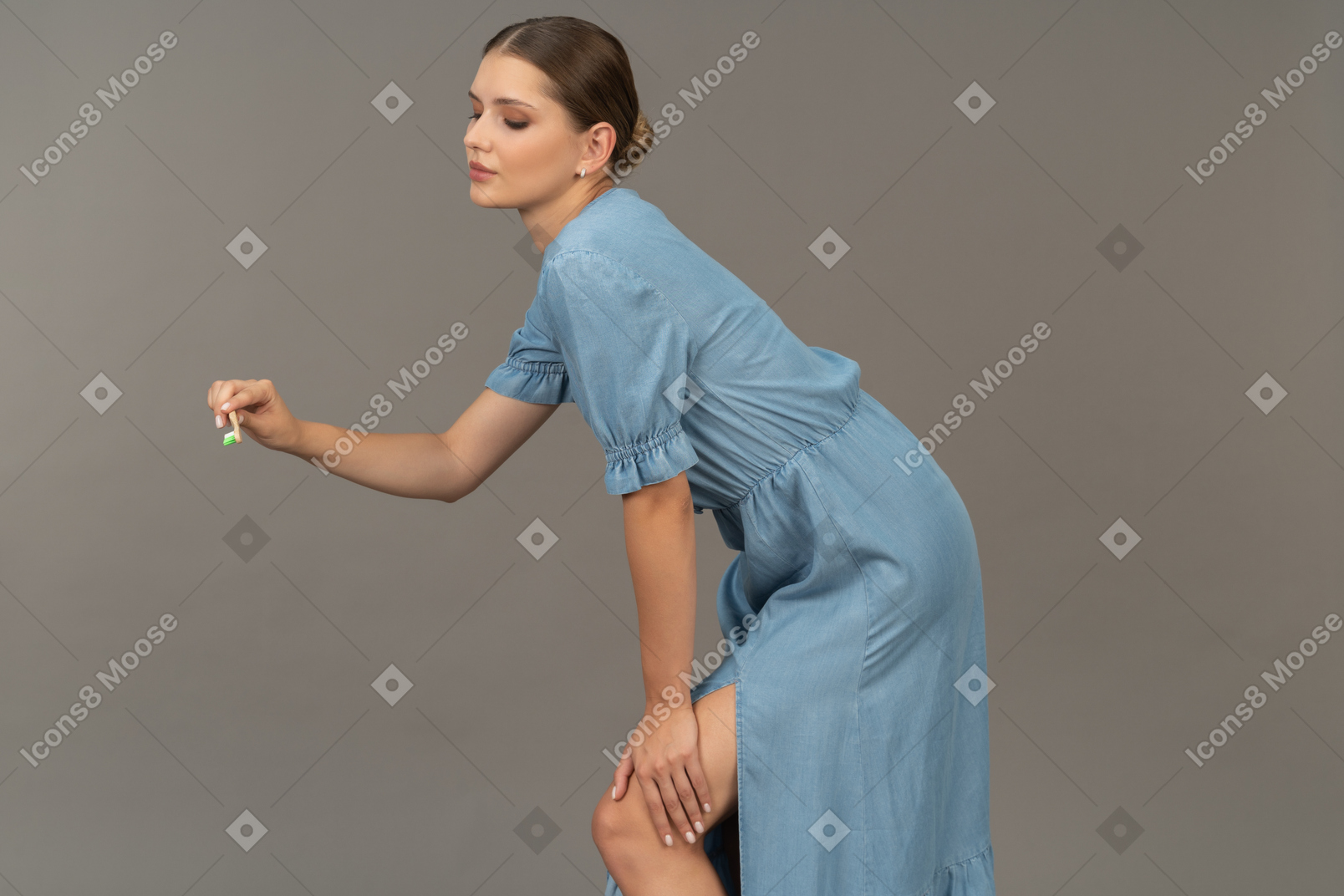 Side view of a young woman in blue dress holding toothbrush & leaning forward