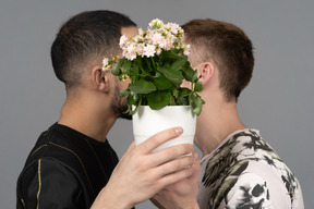 Close-up de dois jovens segurando um vaso de flores para cobrir o rosto