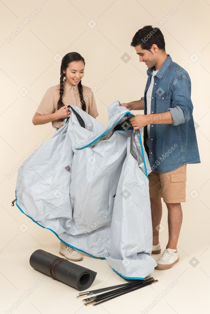 Молодая азиатская женщина и кавказский мужчина устанавливают палатку