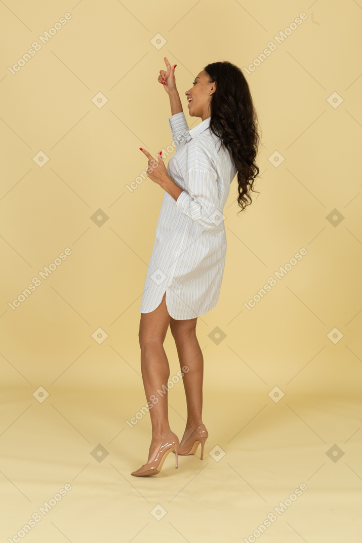 Side view of a screaming dark-skinned young female in white dress pointing fingers up