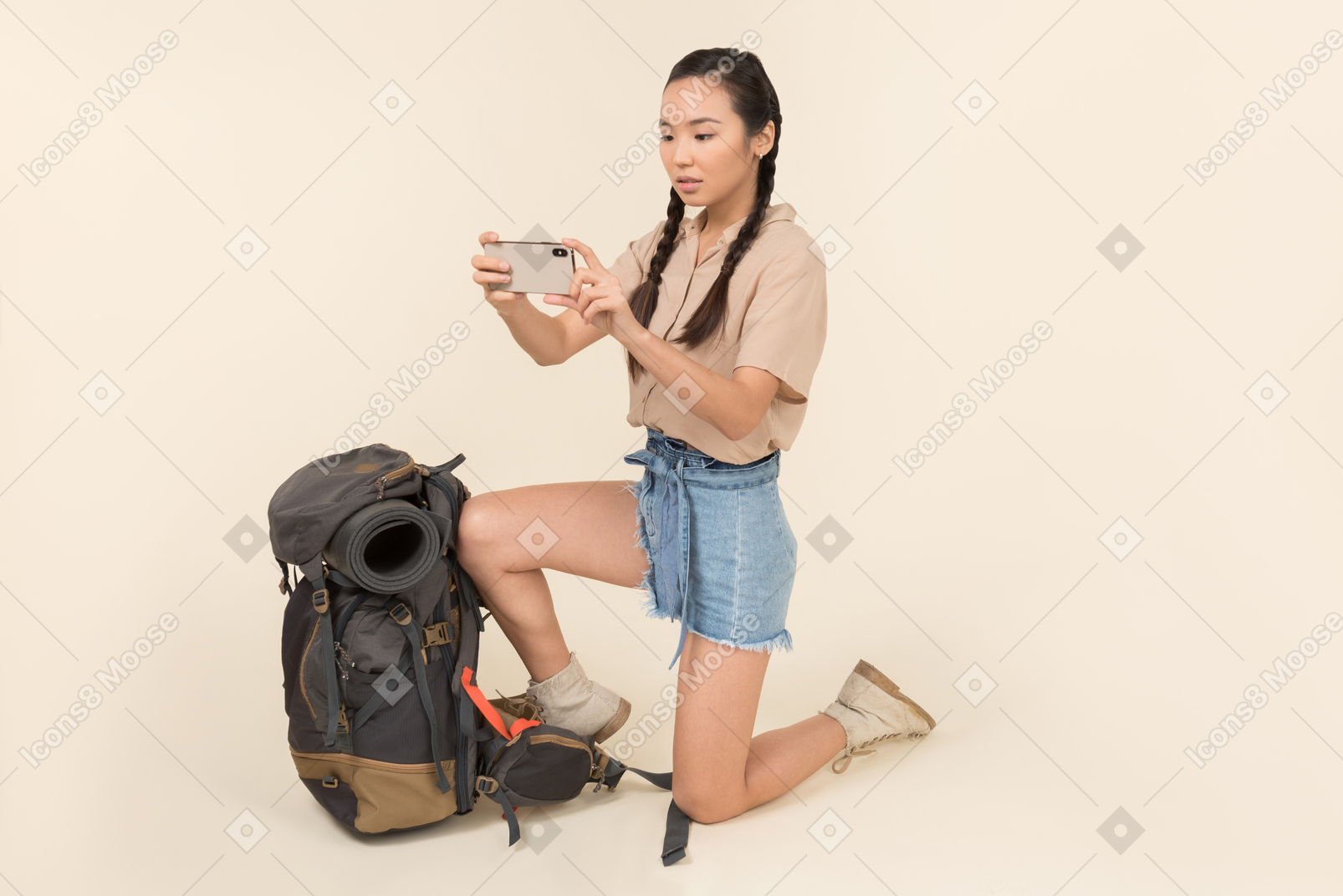 Outraged young asian woman standing near backpack and taking picture with smartphone