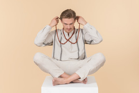 Young caucasian man sitting in lotus pose and putting on necklace