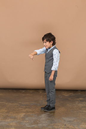 Вид сбоку на мальчика в сером костюме, показывающего большой палец вниз