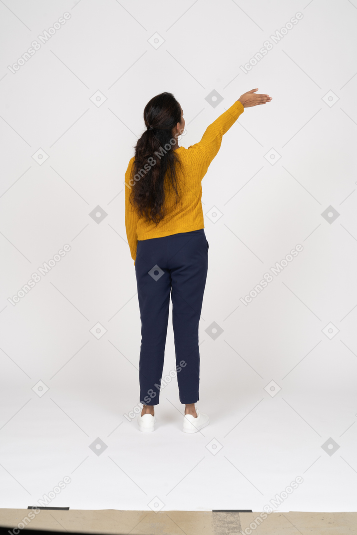 Rear view of a girl in casual clothes standing with raised arm