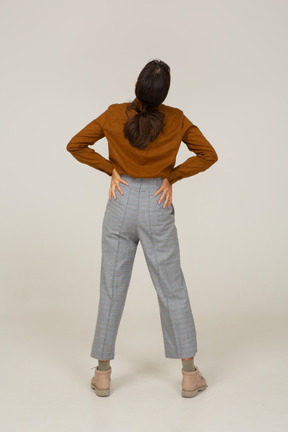 Vista posterior de una joven mujer asiática en calzones y blusa poniendo las manos en las caderas