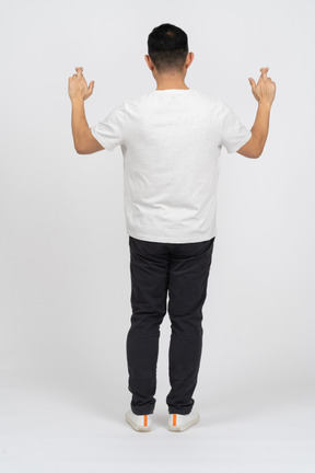 Vista posteriore di un uomo in abiti casual in piedi con le mani alzate e le dita incrociate