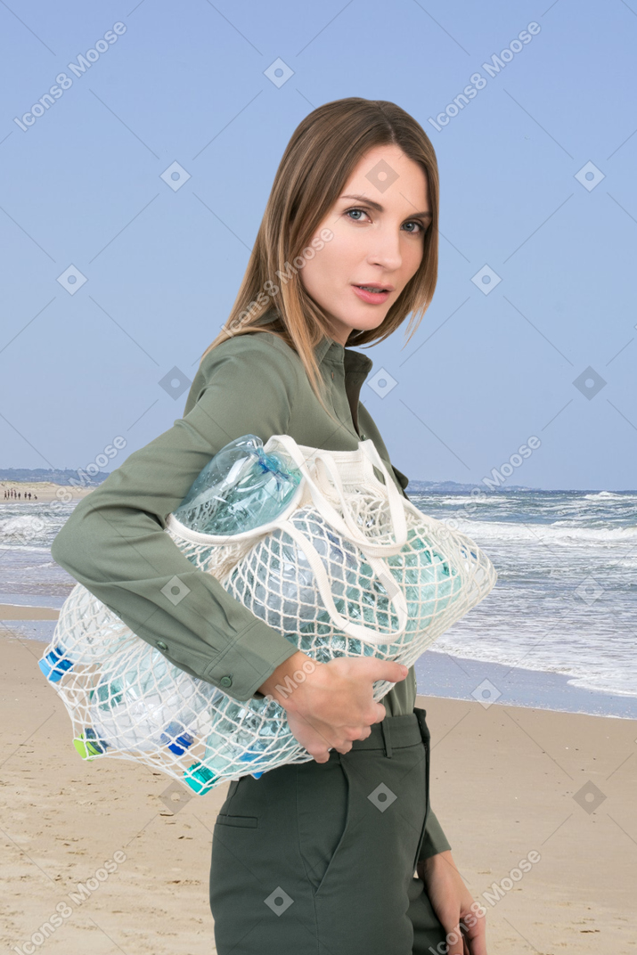 A woman standing on a beach holding a bag