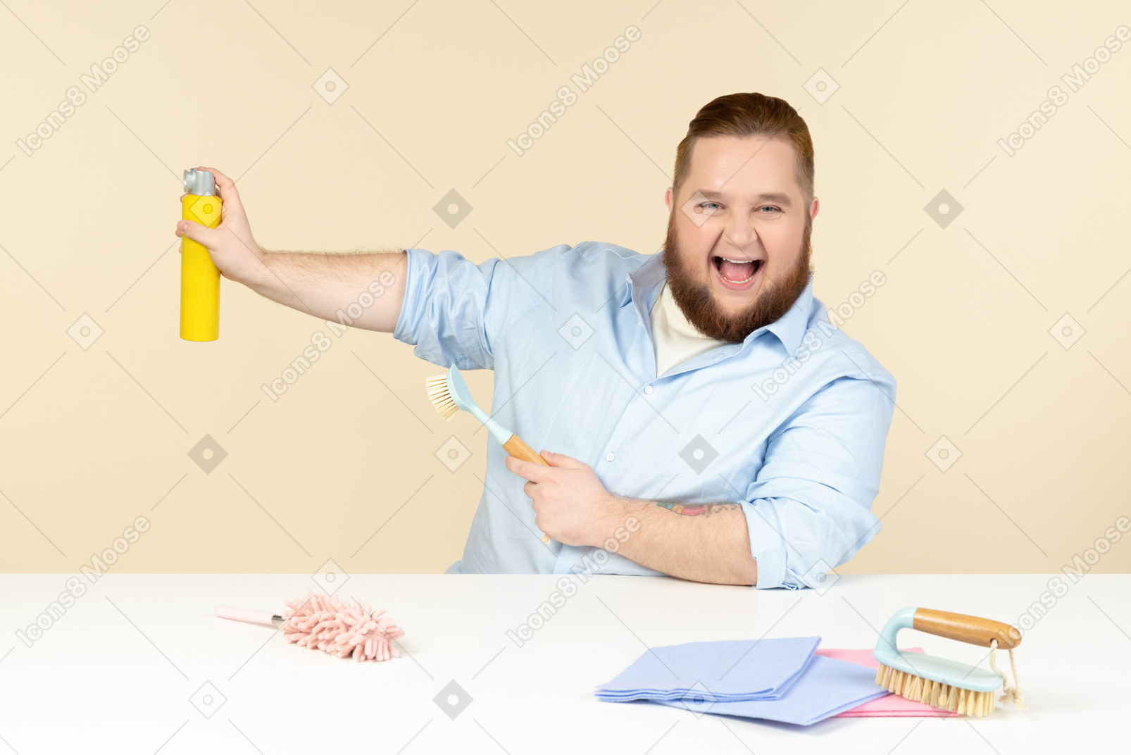 Young overweight man sitting at the table in the profile and holding cleaning equipment