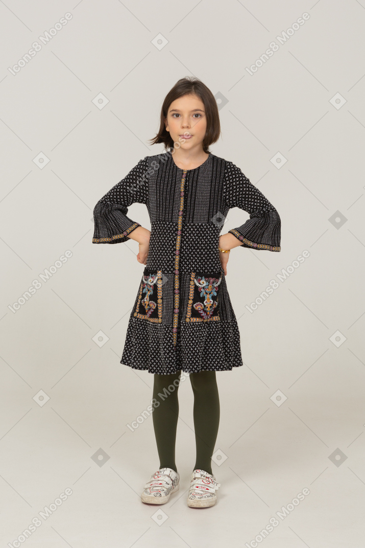 Vista frontale di una bambina divertente in abito che mostra la lingua e mette le mani sui fianchi