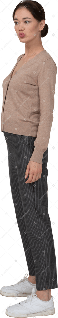 Vista de tres cuartos de una señorita parada quieta en jersey y pantalones poniendo la mano en la cadera y haciendo pucheros