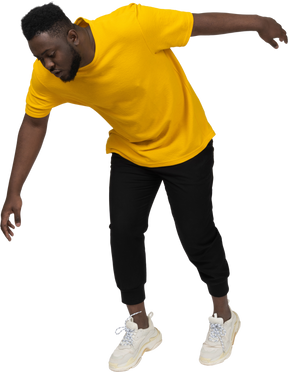 Vista di tre quarti di un giovane uomo dalla pelle scura con indosso una maglietta gialla proteso in avanti e il braccio teso