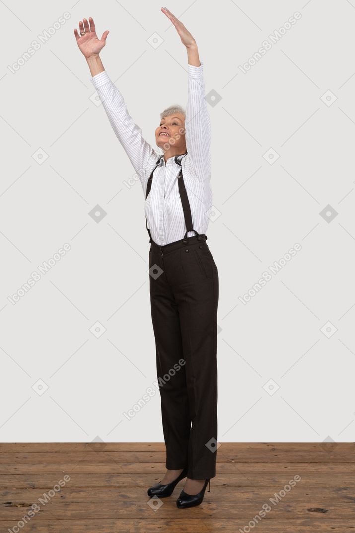 Tre quarti indietro di una vecchia signora in abiti da ufficio alzando le mani