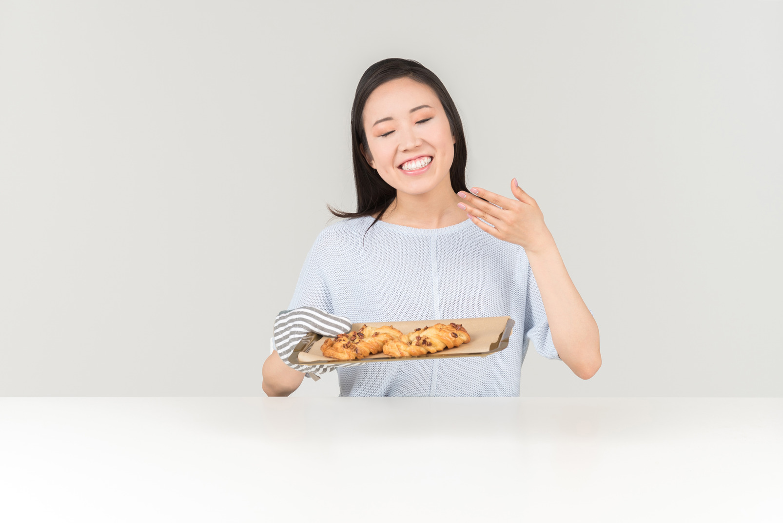 Smiling young asian woman smelling cookies that are on the tray