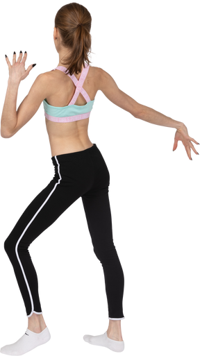 Back view of a teen girl in sportswear raising hands and dancing