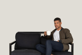 Front view of a young man sitting on a sofa with a cup of coffee