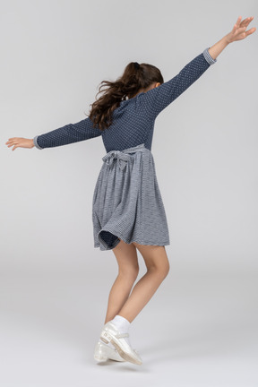 Three-quarter back view of a girl imitating flying like an airplane