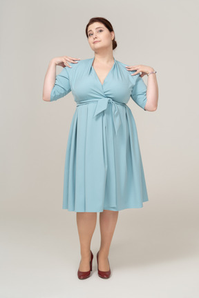 Vista frontal de uma mulher de vestido azul posando com as mãos nos ombros